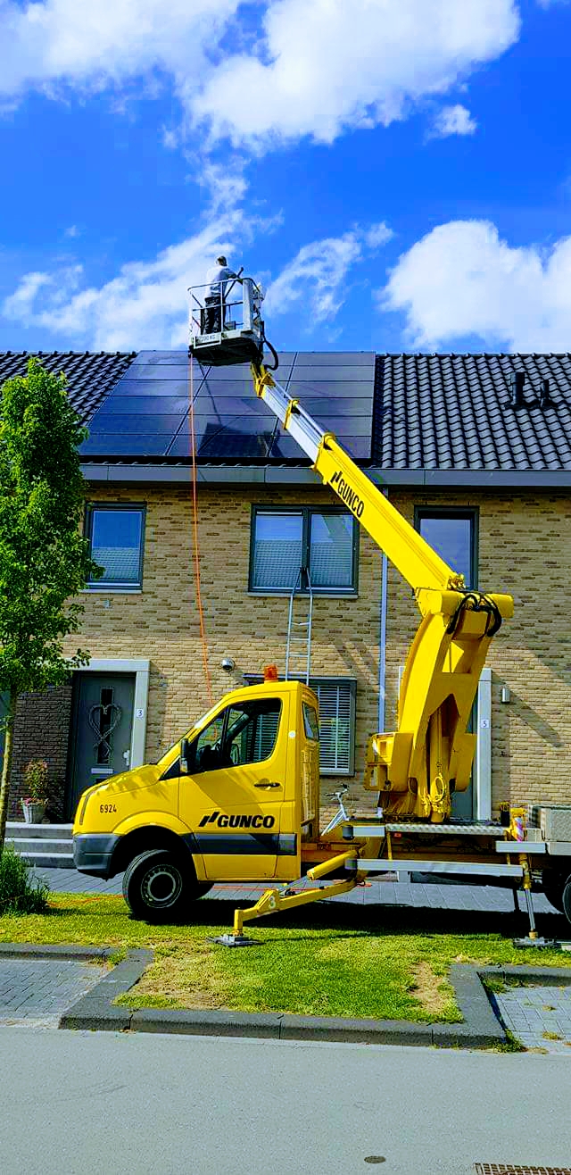 Hoogwerker naast een woning, zonnepanelen op het schuine dak worden gereinigd.