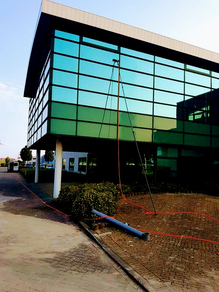 Glazen kantoorgevel die met een telescoopsteel vanaf de grond wordt gewassen.